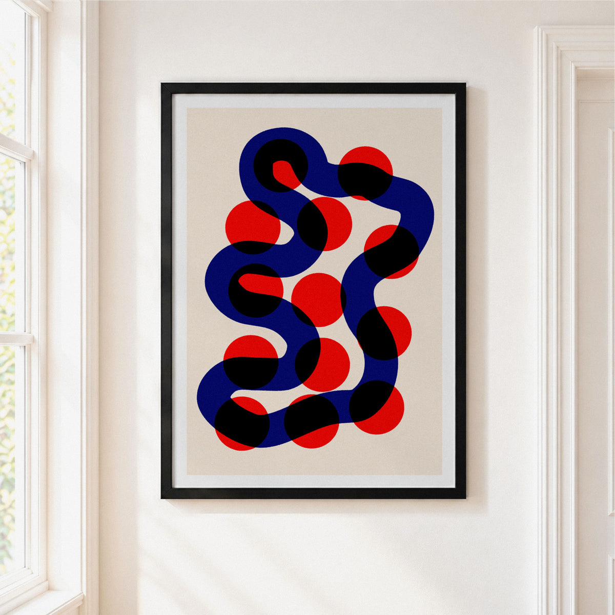Framed abstract wall art hanging on a white wall beside a window. The print shows a wavy dark blue and black line with red circular dots on a light beige background, enclosed in a black frame with a white mat.
