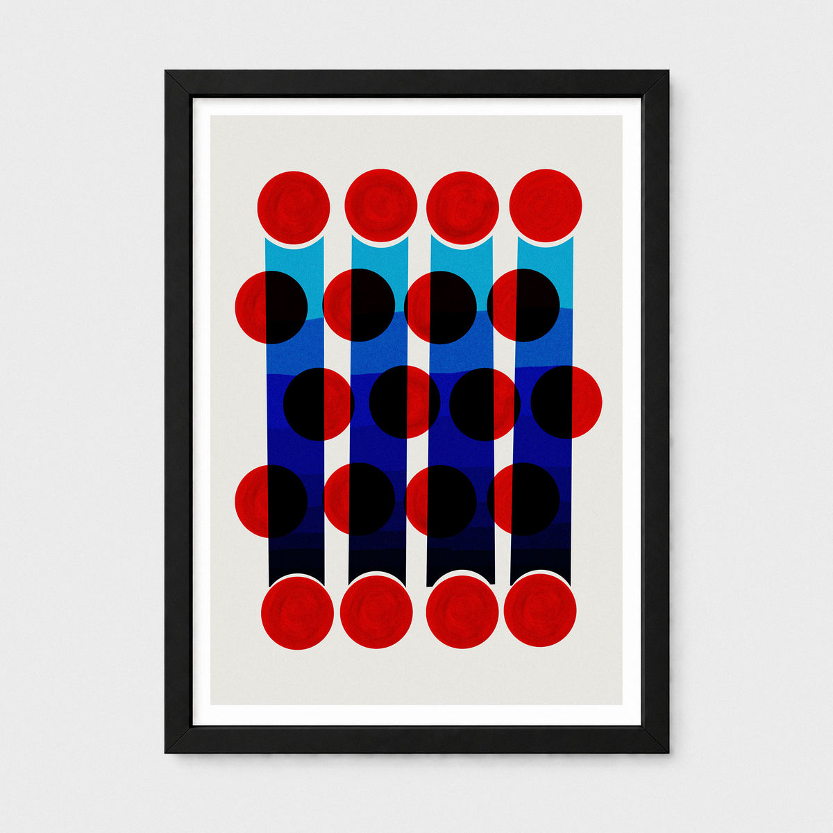 Framed abstract geometric wall art featuring red, black, and blue circular and rectangular shapes on a light background, presented in a black frame with a white mat against a light gray wall.