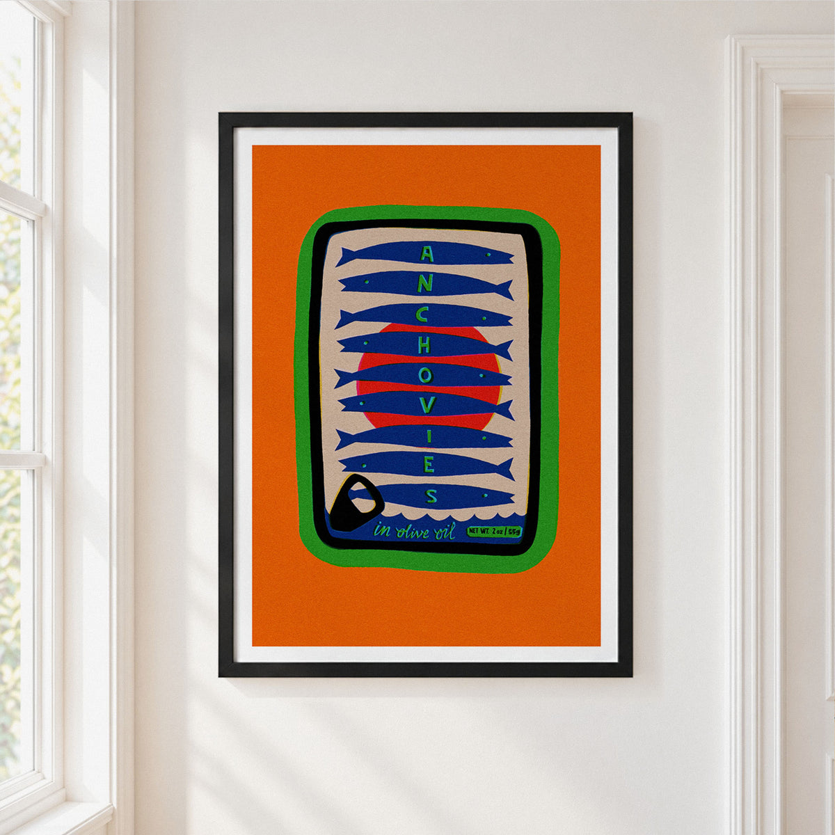 A framed art print featuring a stylized sardine can illustration with the words 'ANCHOVIES' and 'IN OLIVE OIL' on an orange background, hung on a white wall next to a window.