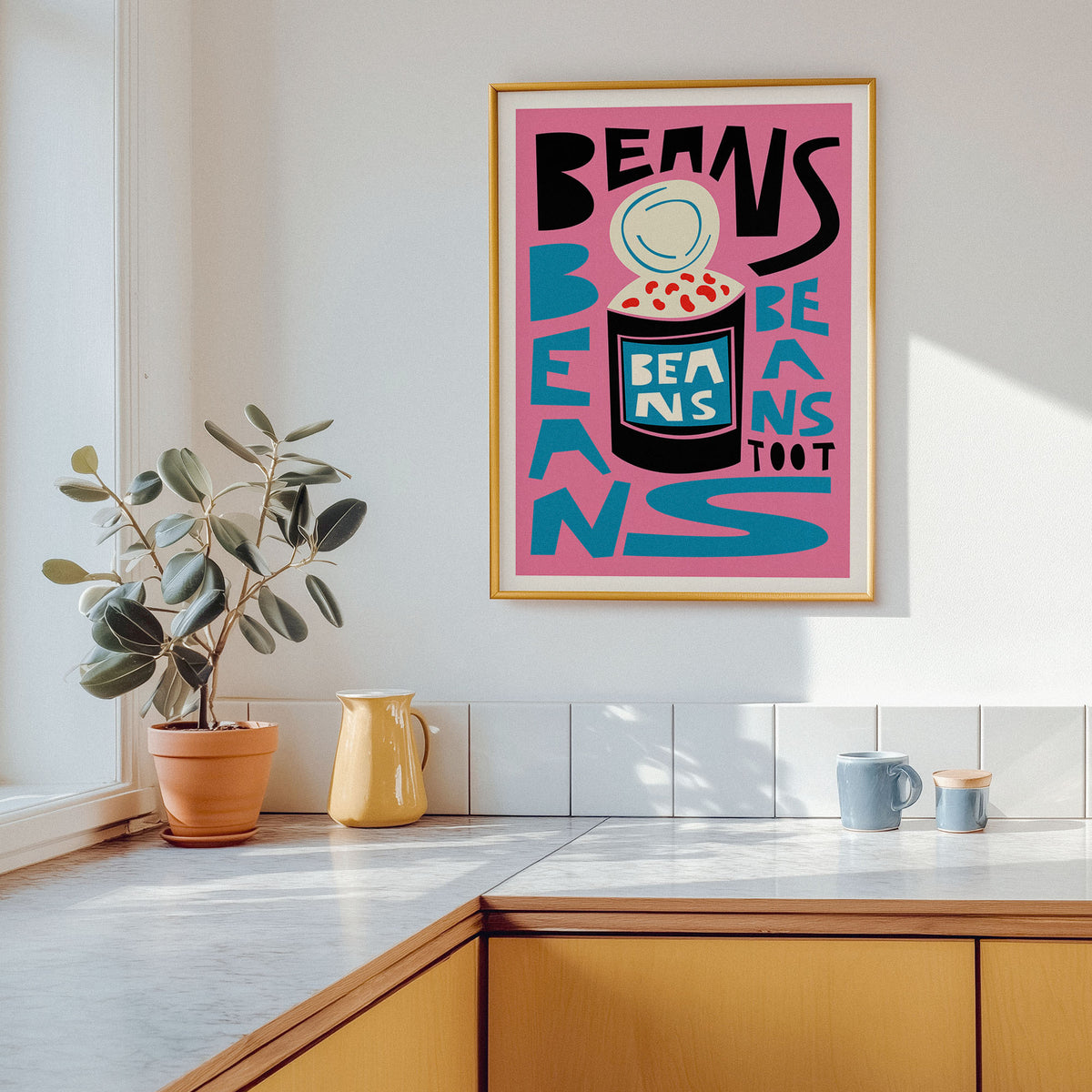 A framed art print featuring a colorful retro-style illustration with the words 'BEANS TOOT' and 'BEANS' in bold black and teal lettering on a pink background, hanging on a white kitchen wall above a counter with a potted plant and mugs.