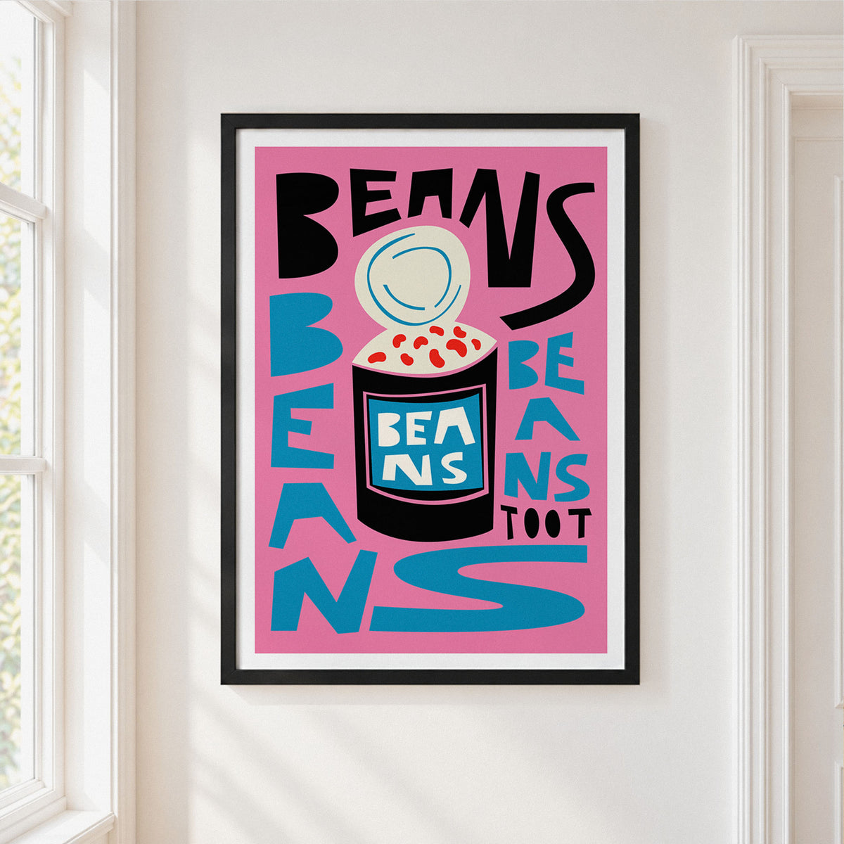 A framed art print featuring a bold graphic design with the words 'BEANS TOOT' and a stylized bean jar illustration, hung on a white wall next to a window.