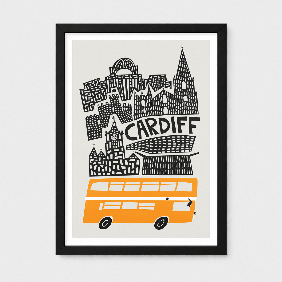 A framed art print featuring a stylized black line-art skyline of Cardiff with the word 'CARDIFF' in the center and an orange double-decker bus at the bottom, shown against a light gray background.