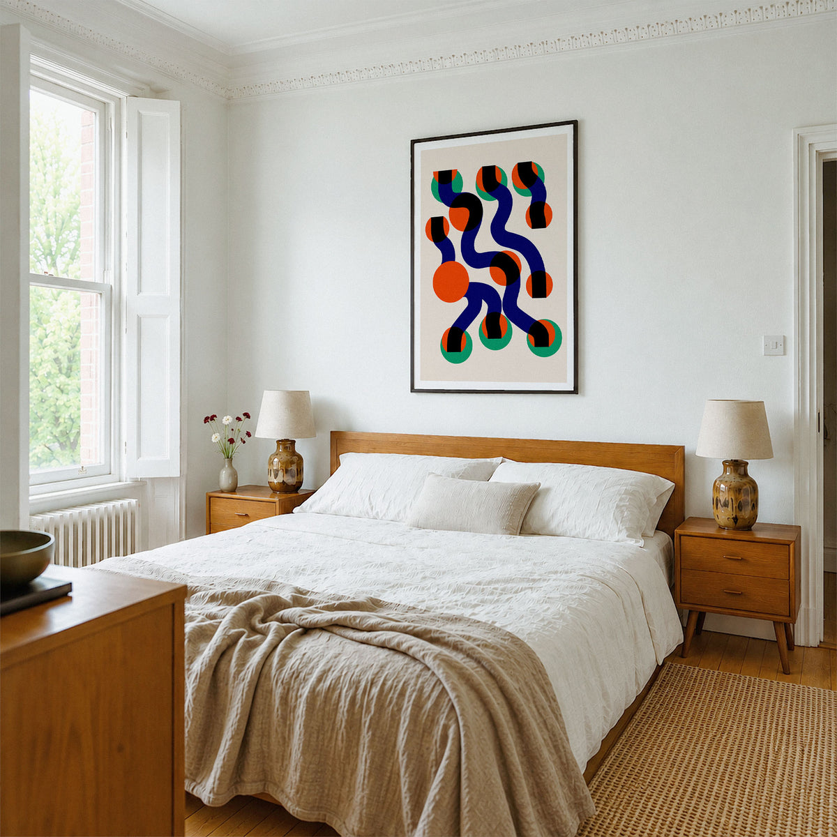A modern bedroom featuring a colorful abstract wall art print with wavy organic shapes in navy, orange, red, and green on a cream background. The print is displayed above a wooden bed frame with white bedding and a beige linen throw.
