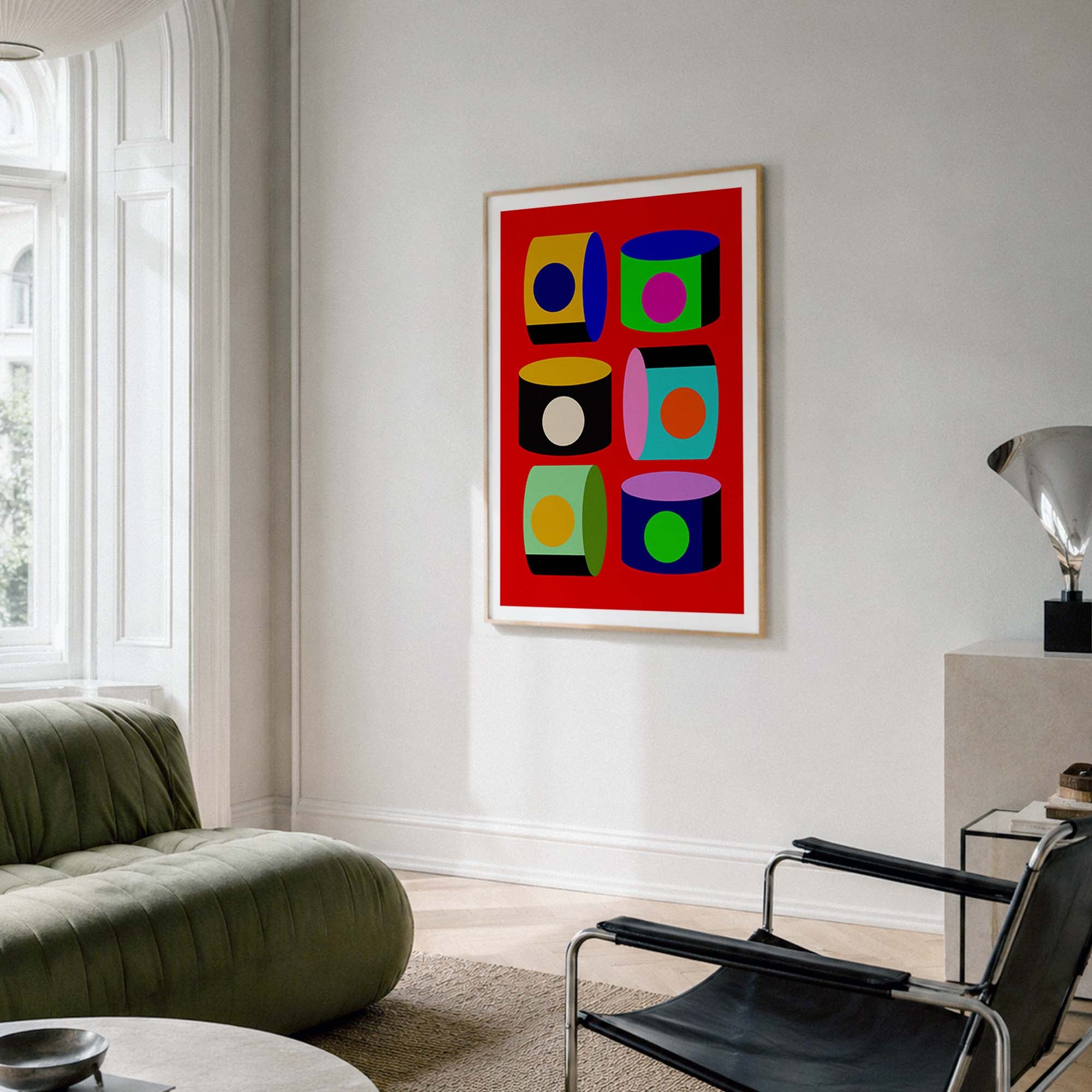 A framed abstract pop art print with a bold red background and colorful geometric shapes hangs on a light gray wall in a modern living room setting.
