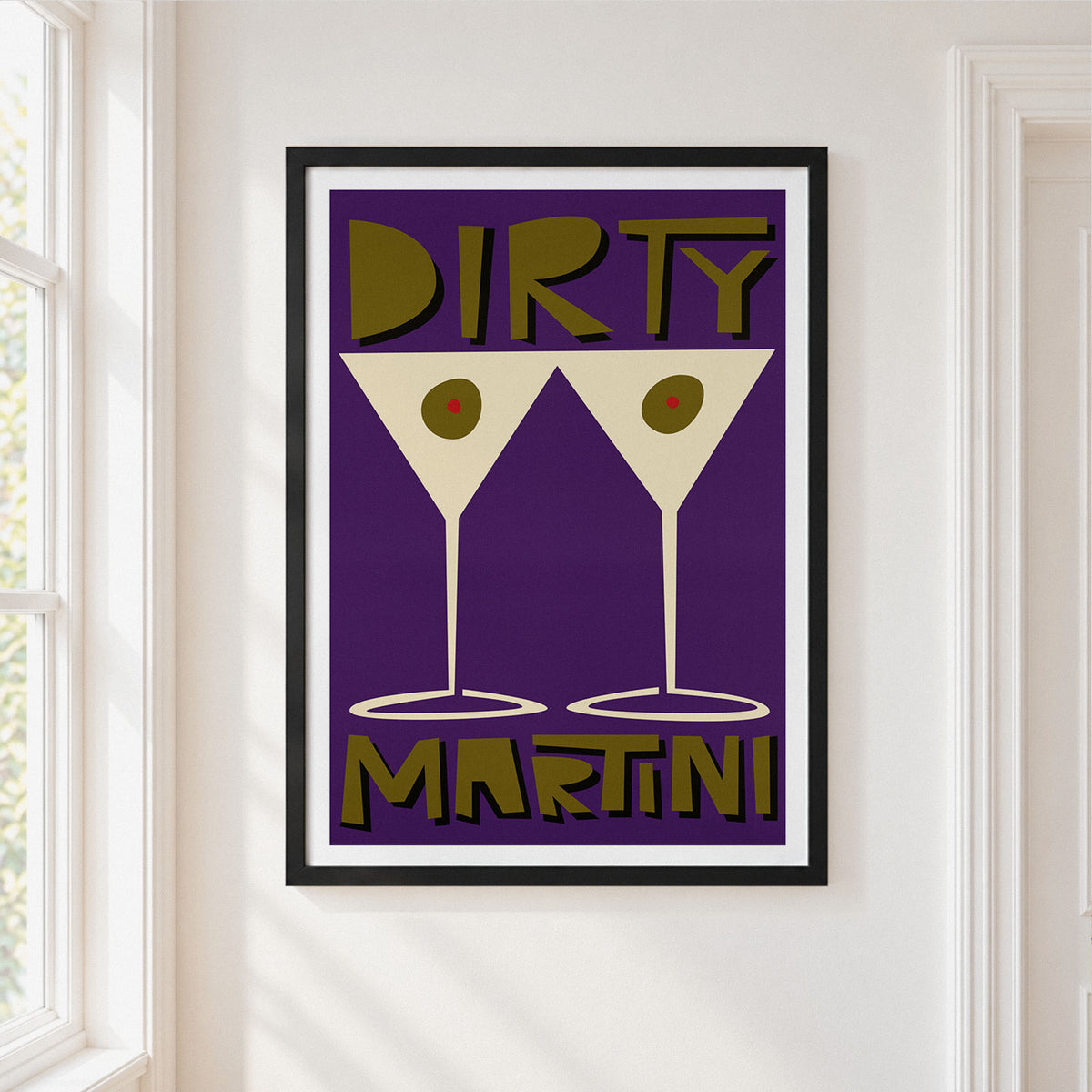 A framed art print featuring a retro design with the words 'DIRTY MARTINI' and two martini glasses on a purple background, hanging on a white wall next to a window.