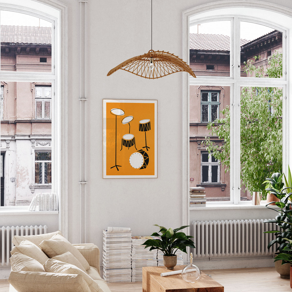 A framed art print featuring a minimalist orange, black, and white drum set illustration hangs on a white wall in a bright, modern living room with large windows, a rattan pendant light, and plants.