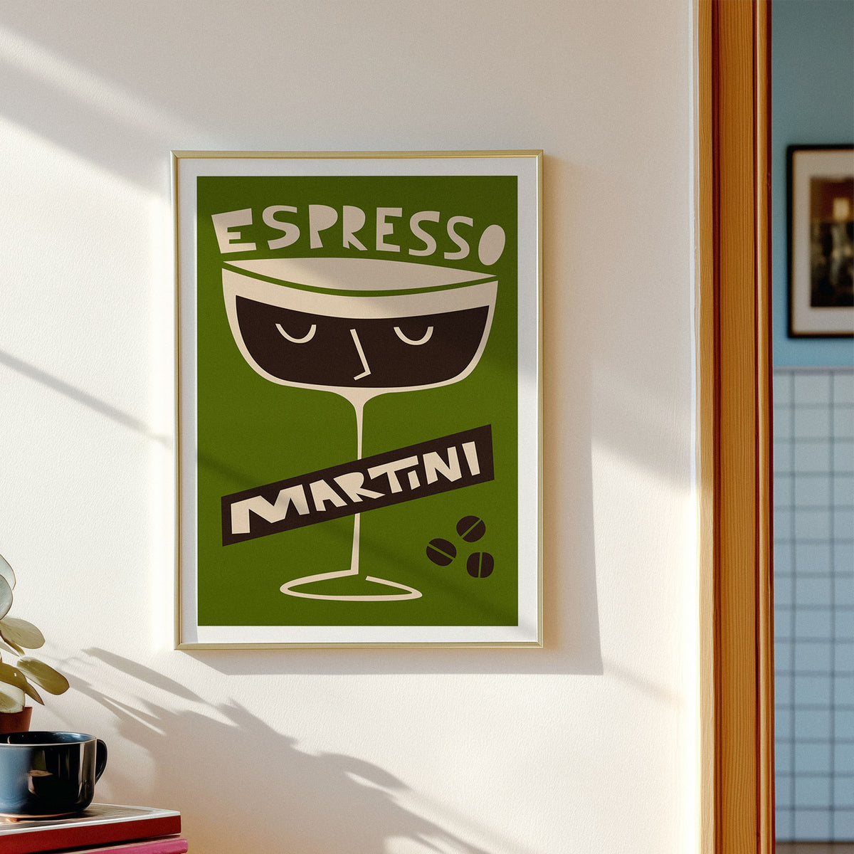 A framed vintage-style poster reading 'ESPRESSO MARTINI' hangs on a light wall above a wooden dining table with chairs in a real interior setting.