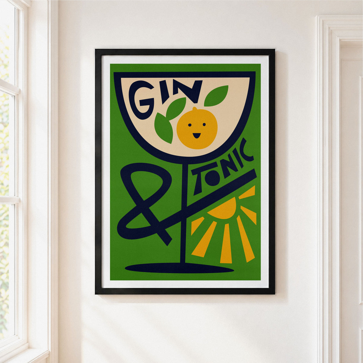 Framed wall art poster hanging on a white wall beside a window. The artwork features a stylized green cocktail glass with the words “GIN & TONIC,” a yellow smiling orange, and a yellow sun in a retro graphic design.