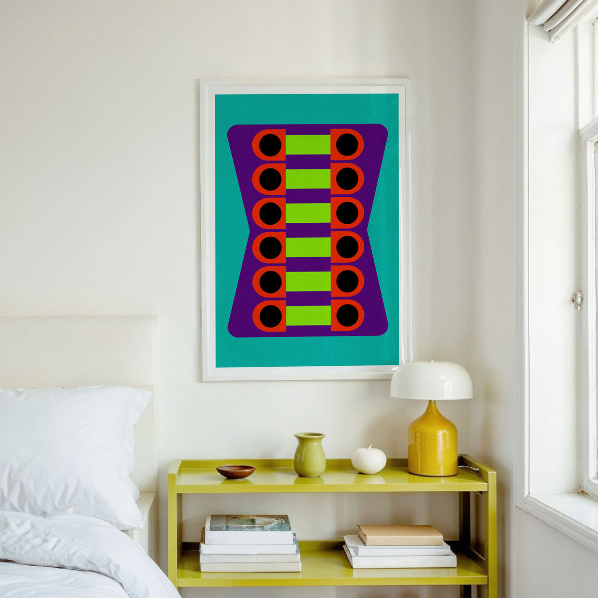 A framed abstract art print featuring colorful geometric circles on a teal background, hanging on a white wall above a yellow shelf in a bright bedroom setting.