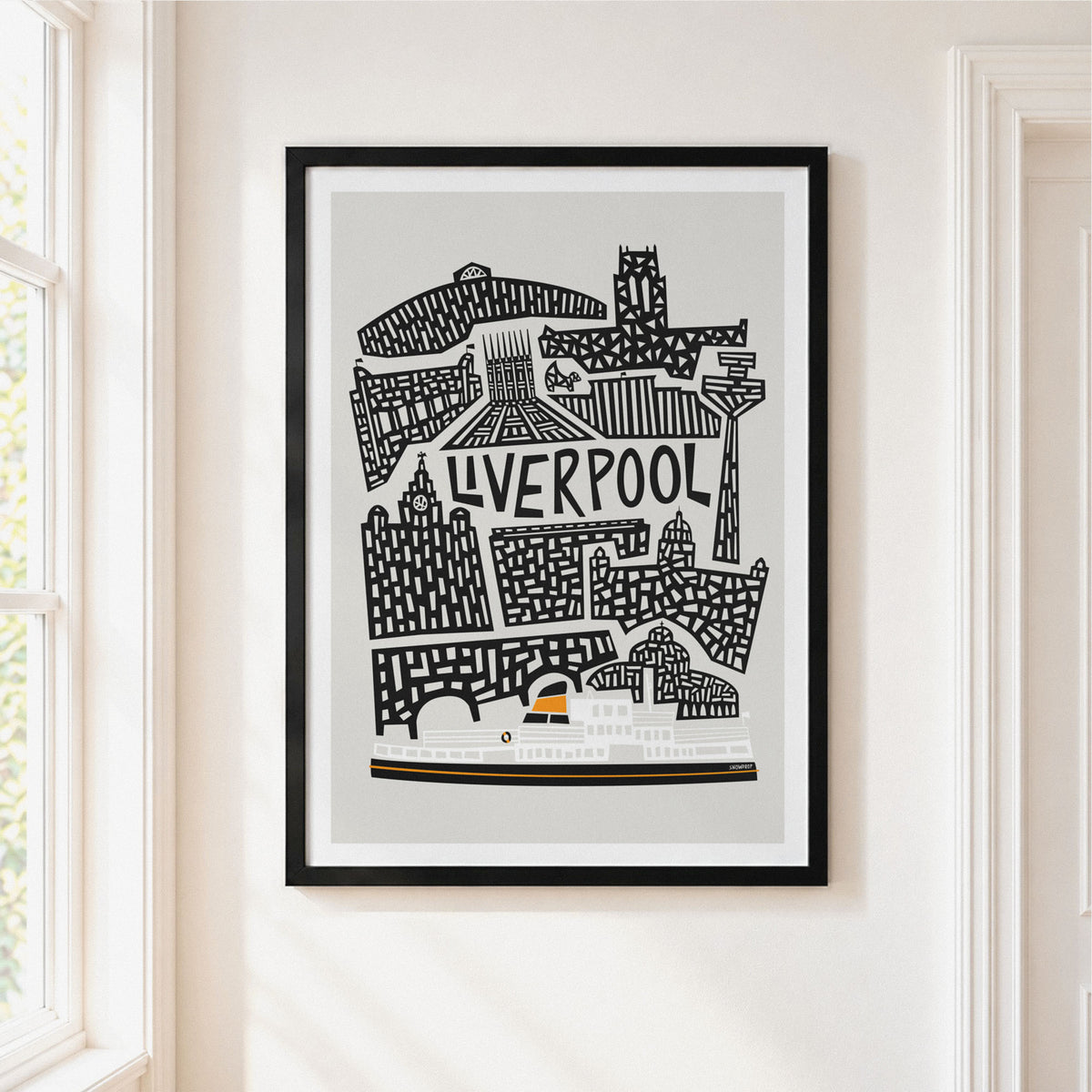 A framed Liverpool cityscape art print with black line art on a light gray background, hanging on a cream-colored wall next to a window.