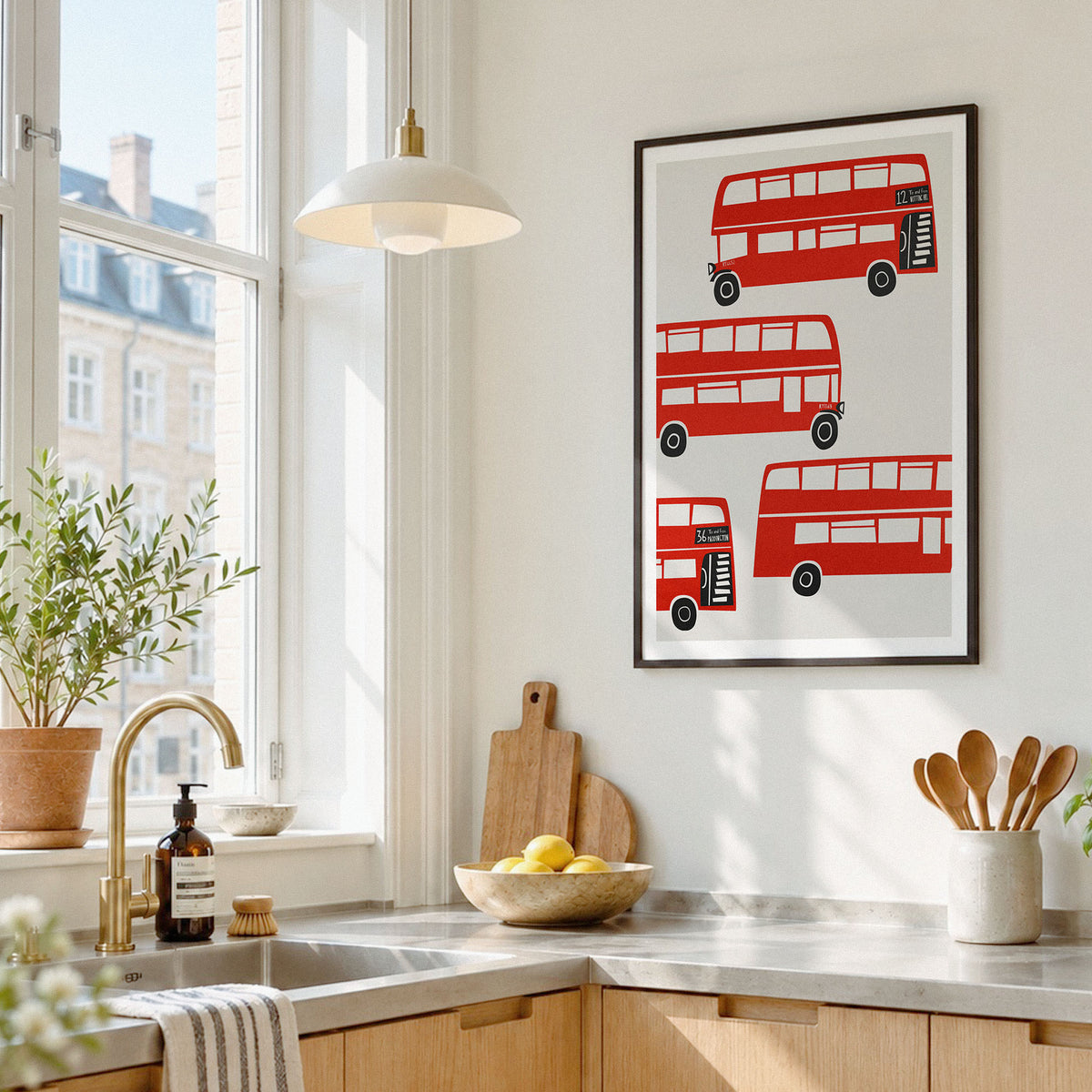 A framed wall art print featuring four red double-decker buses on a white background, displayed in a bright, modern kitchen above a marble countertop.
