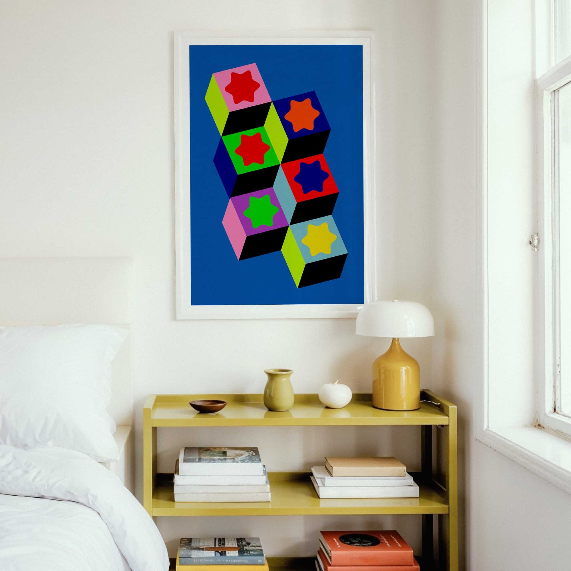 Colorful geometric abstract art on a wall above a yellow shelf with books and a lamp.