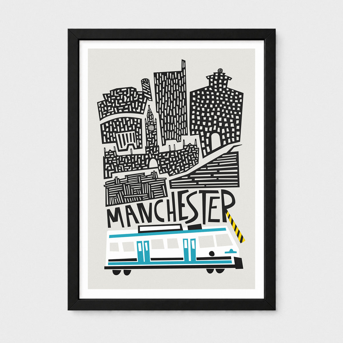 A framed art print featuring a stylized black-and-white illustration of Manchester landmarks above a rwhite and blue tram, shown against a light grey background.