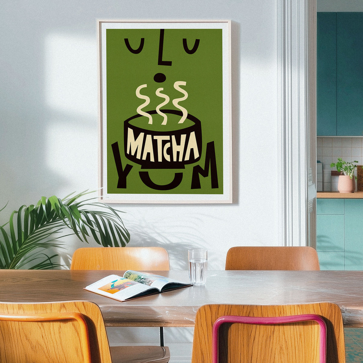 A framed art print featuring a stylized green and black illustration of a matcha bowl with the word 'MATCHA' inside, hanging on a light gray wall in a modern dining room setting.