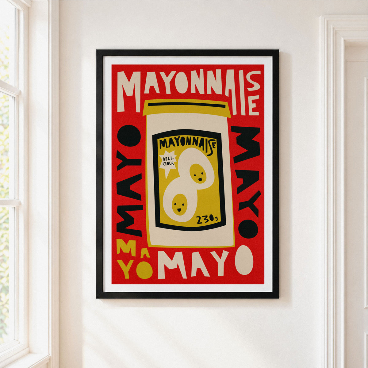 A framed vintage-style mayonnaise poster hanging on a white wall in a bright room. The poster features bold red, cream, yellow, and black graphics with the word MAYONNAISE and a jar illustration.