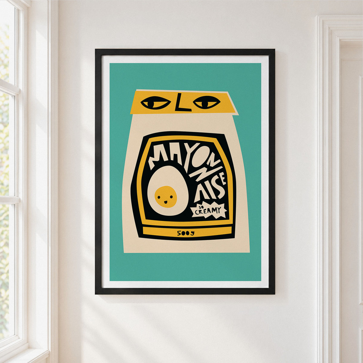 A framed art print featuring a stylized mayonnaise jar illustration with a cream-colored body, black label, yellow accents, and a teal background, hung on a white wall next to a window.