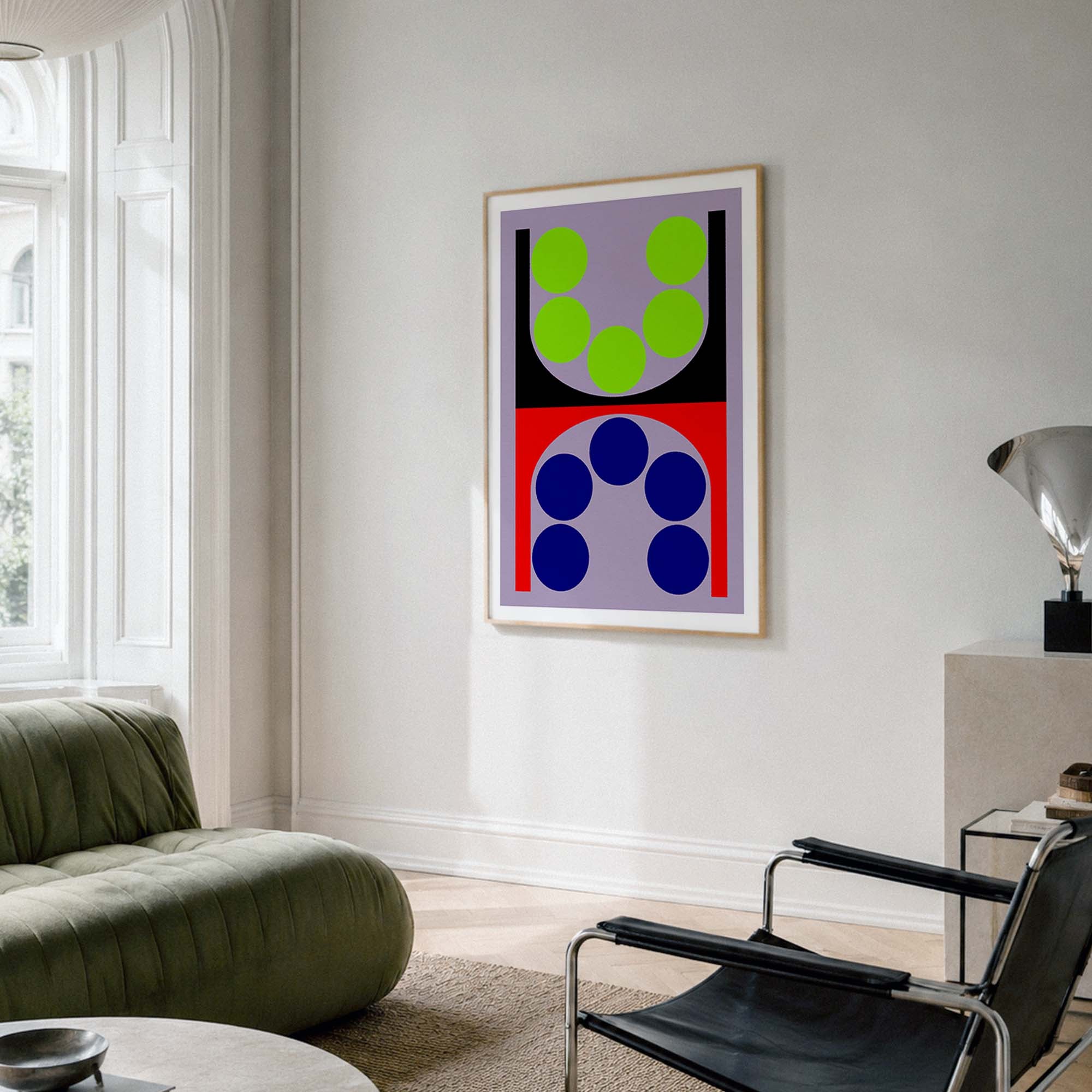 A framed abstract geometric wall art print hangs on a white wall in a modern living room. The artwork features bold shapes in lime green, navy blue, red, black, and lavender.