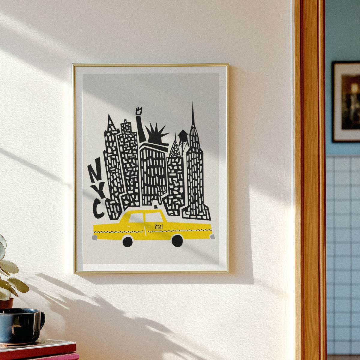 A framed art print featuring a stylized New York skyline with a yellow taxi and black architectural details on a light gray background, hung on a cream-colored wall next to a window.