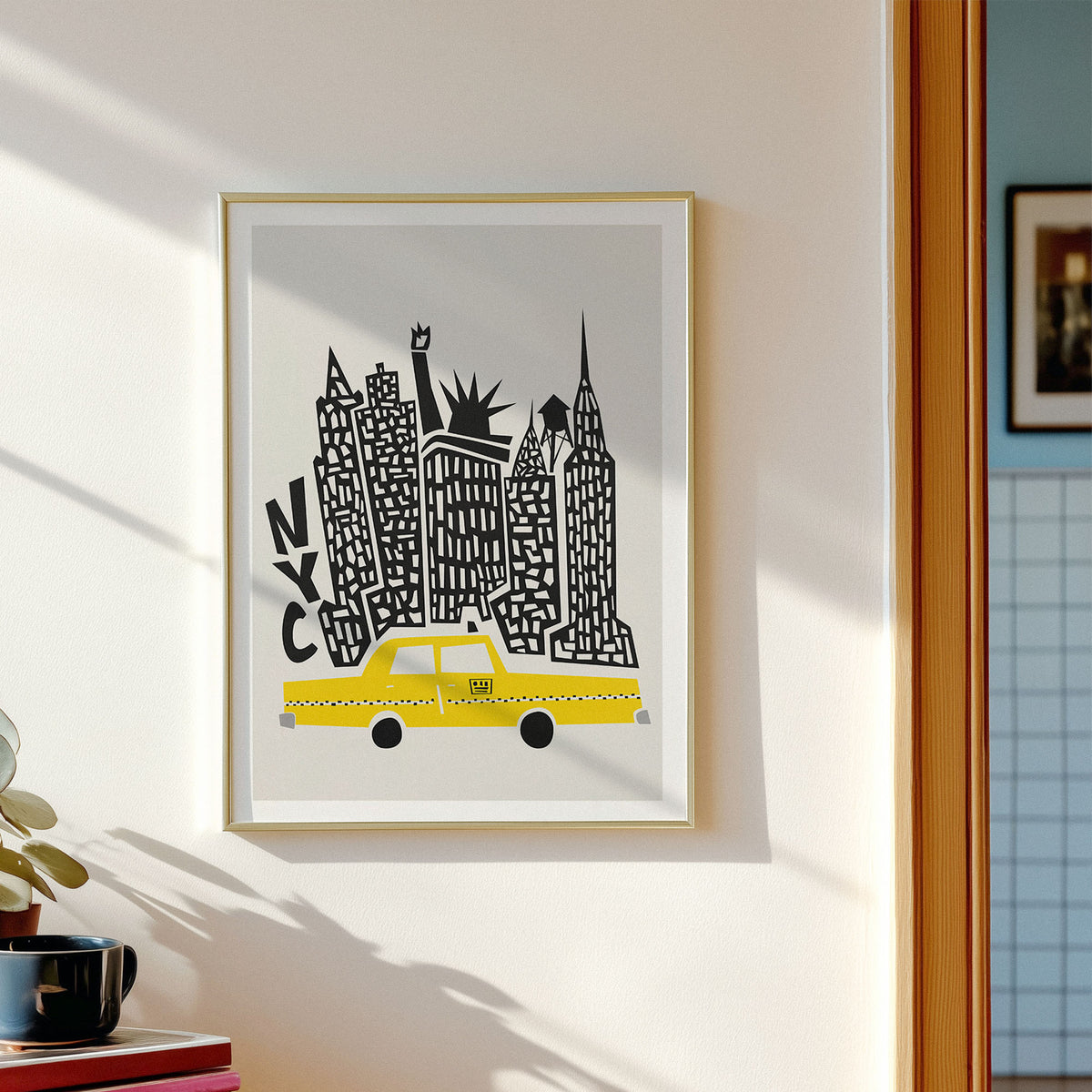 A framed art print featuring a stylized New York skyline with a yellow taxi and black architectural details on a light gray background, hung on a cream-colored wall next to a window.