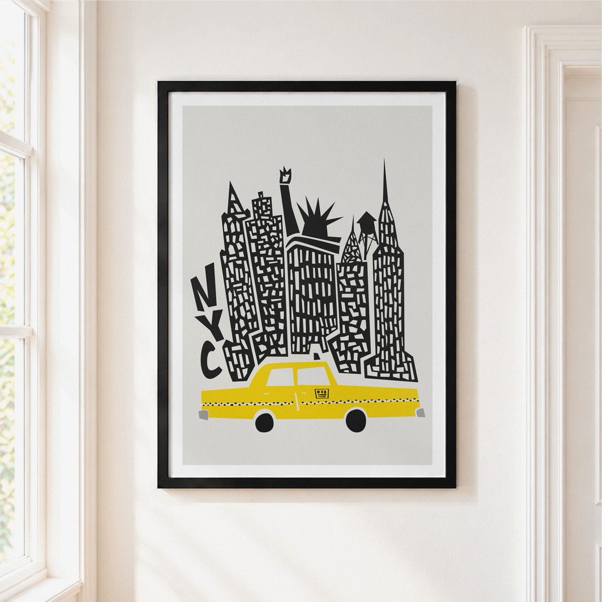 A framed art print featuring a stylized New York skyline with a yellow taxi and black architectural details on a light gray background, hung on a cream-colored wall next to a window.