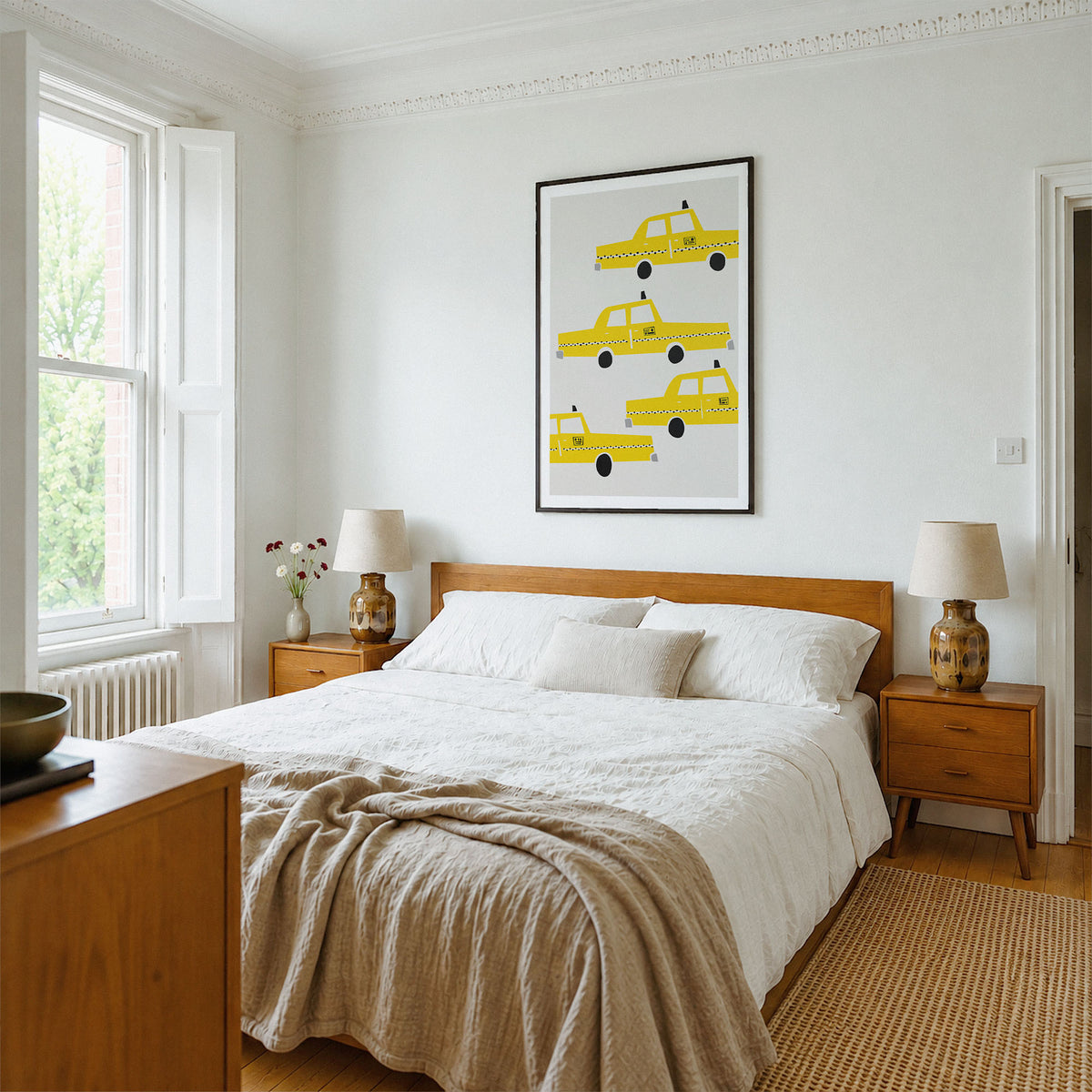 A styled bedroom featuring a framed wall art print with yellow taxi illustrations above a wooden bed. The room has white walls, a wooden headboard and nightstands, matching lamps, a beige textured throw blanket, and a woven rug.