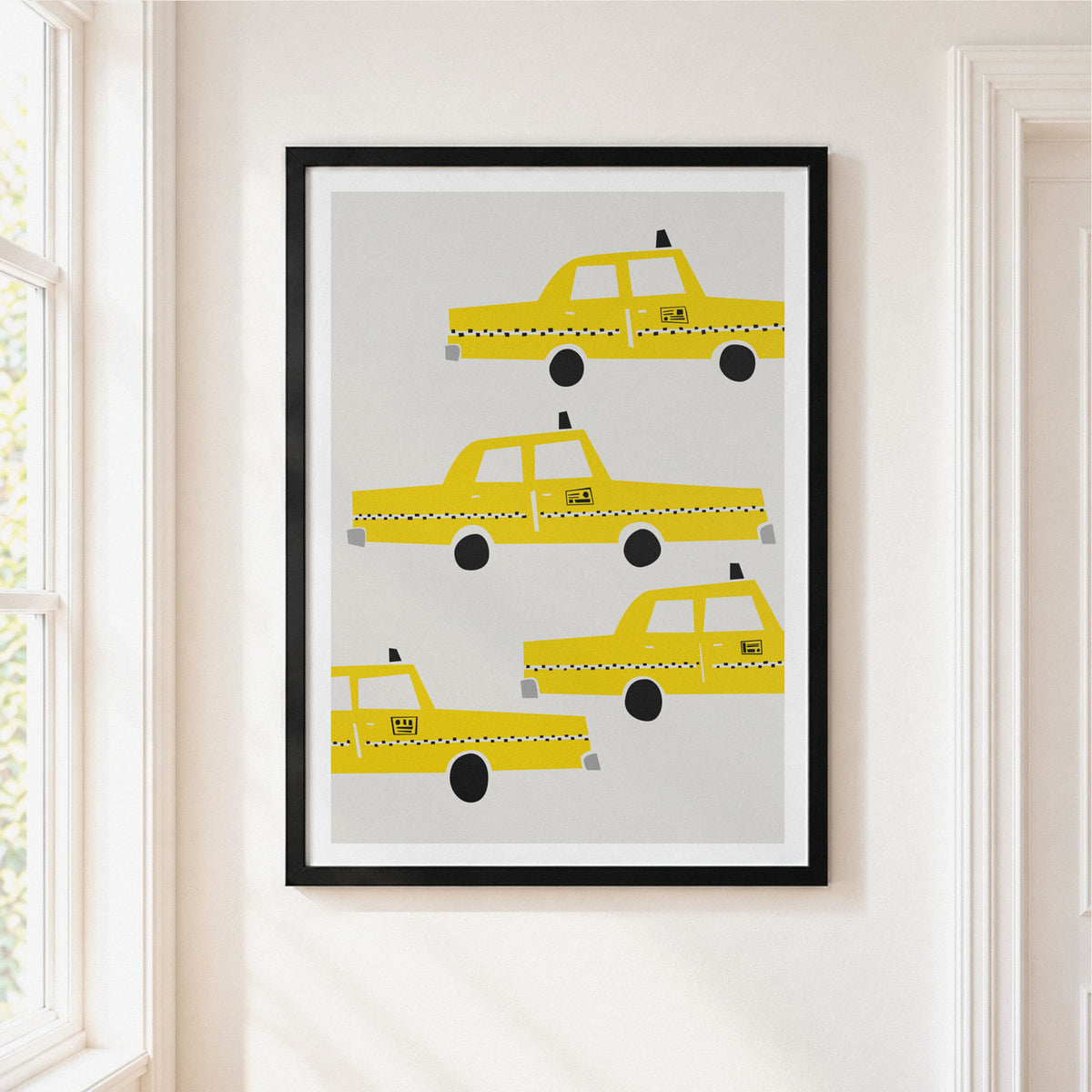 Framed wall art featuring four yellow taxi illustrations on a light gray background, hung on a white wall next to a window.
