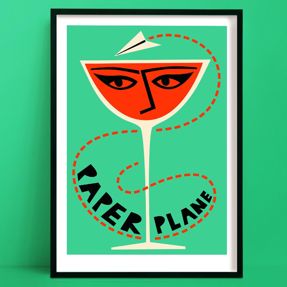 A bold paper plane cocktail print featuring a vivid orange drink in a coupe glass, illustrated with a stylised face and topped with a flying paper plane, all set against a mint green backdrop.