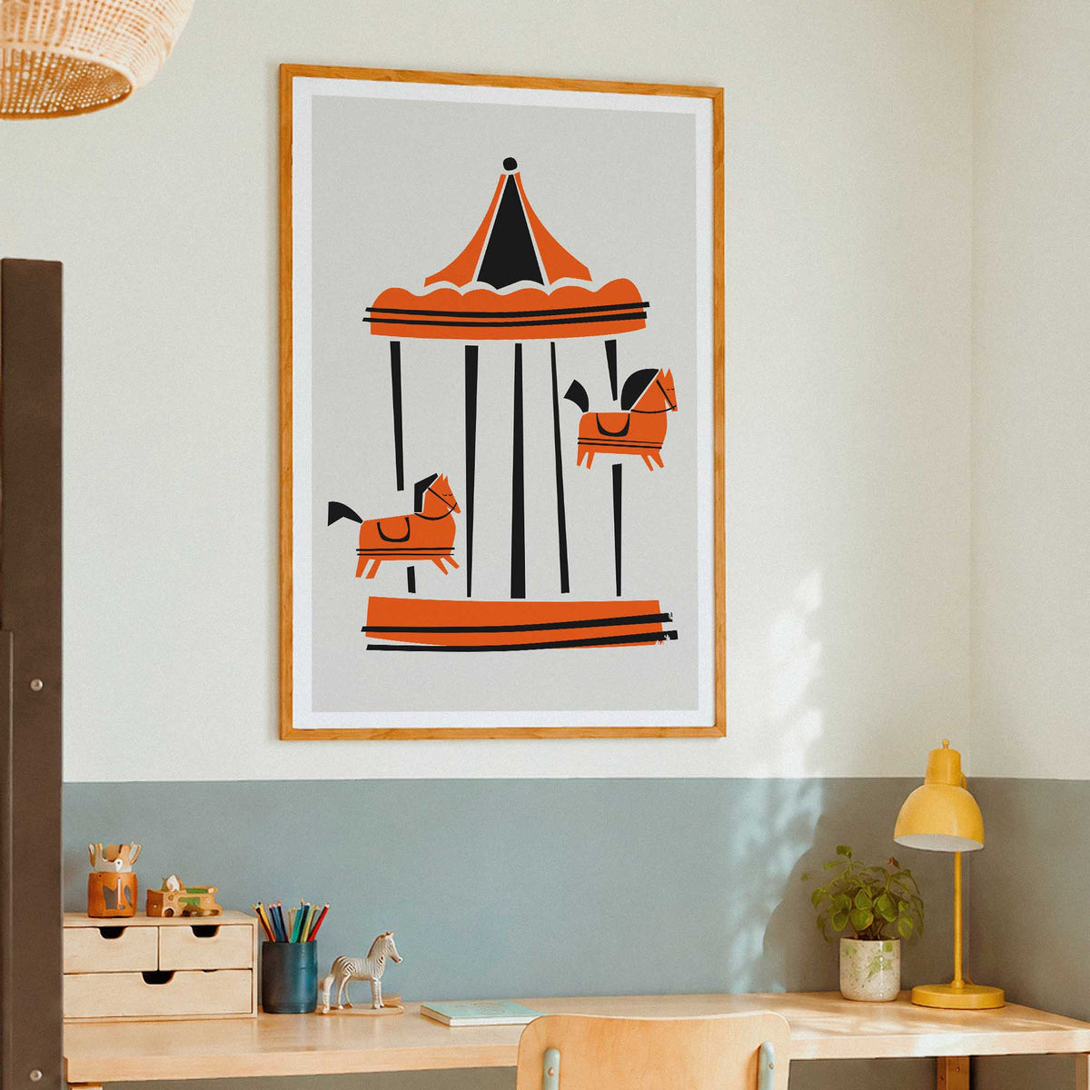 A framed art print of a Parisian carousel illustration hanging on a wall above a wooden desk in a modern room setting.