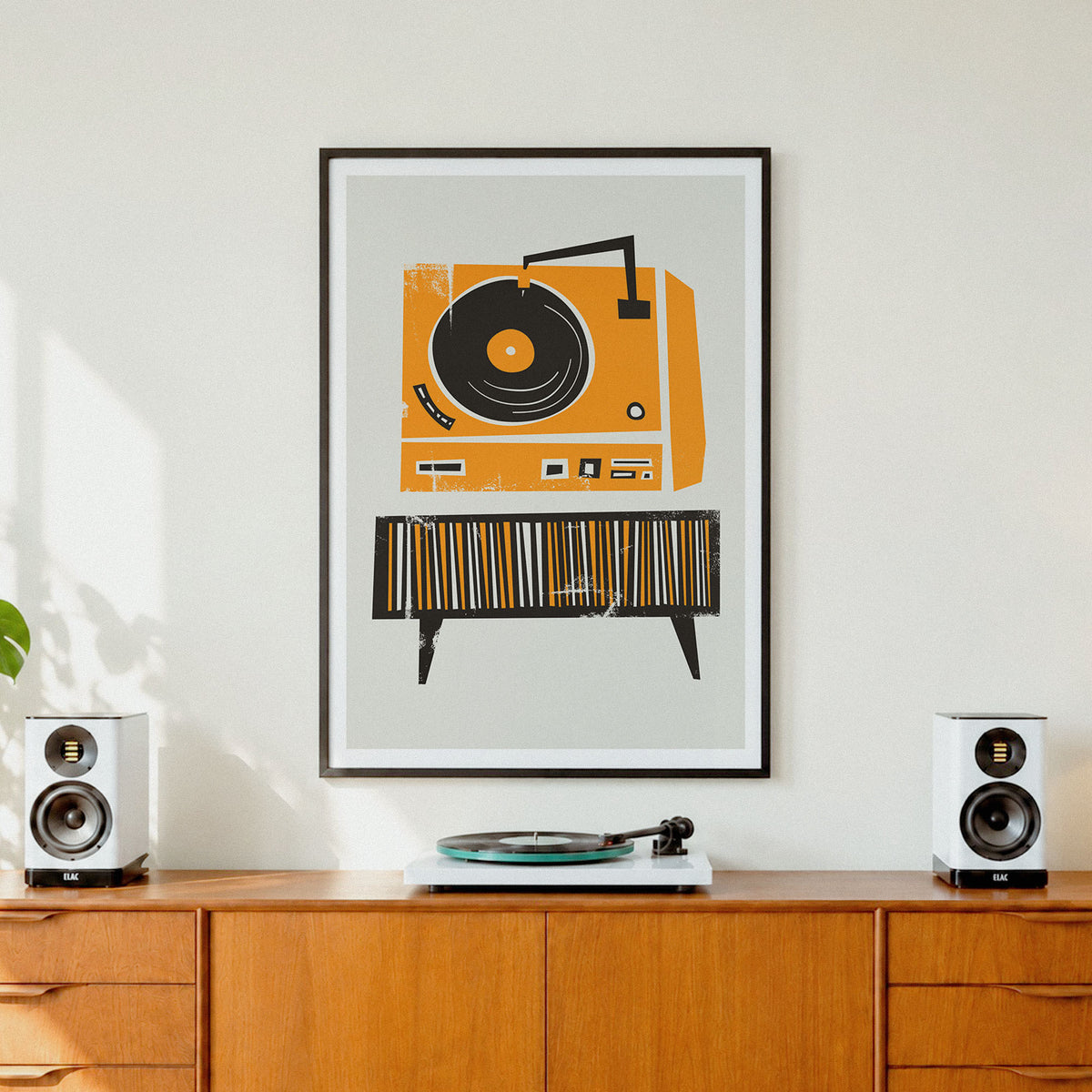 A framed art print featuring a retro orange and black record player illustration, displayed on a wall above a wooden credenza with speakers and a record turntable.