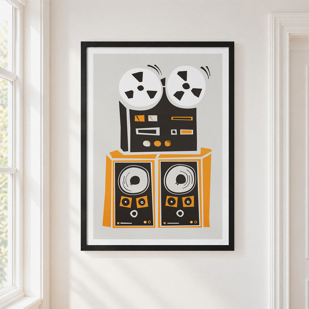 A framed art print featuring a retro graphic of a reel-to-reel tape machine and two speakers in black, orange, and white, displayed on a warm off-white wall next to a window.