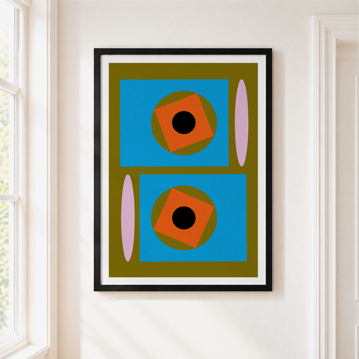 A framed abstract geometric art print hanging on a white wall next to a window. The print features a mid-century modern design with blue rectangles, orange rotated squares, olive green circles, pink vertical ovals, and black centers, all enclosed in a black frame with a white mat.