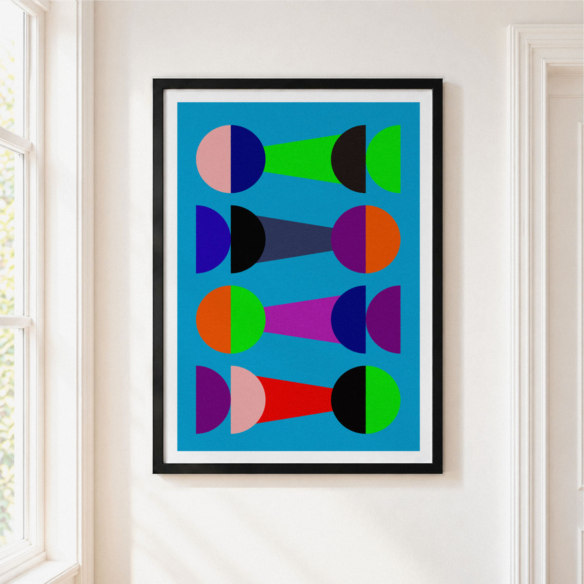 A framed abstract art print featuring colorful geometric shapes on a bright blue background, hung on a white wall next to a window.