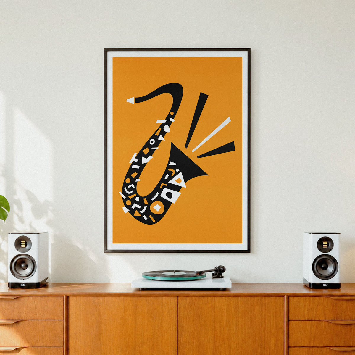 A framed minimalist art print featuring a black saxophone with geometric patterns on a warm orange background, displayed on a wooden cabinet in a modern living room setting with speakers and a turntable.