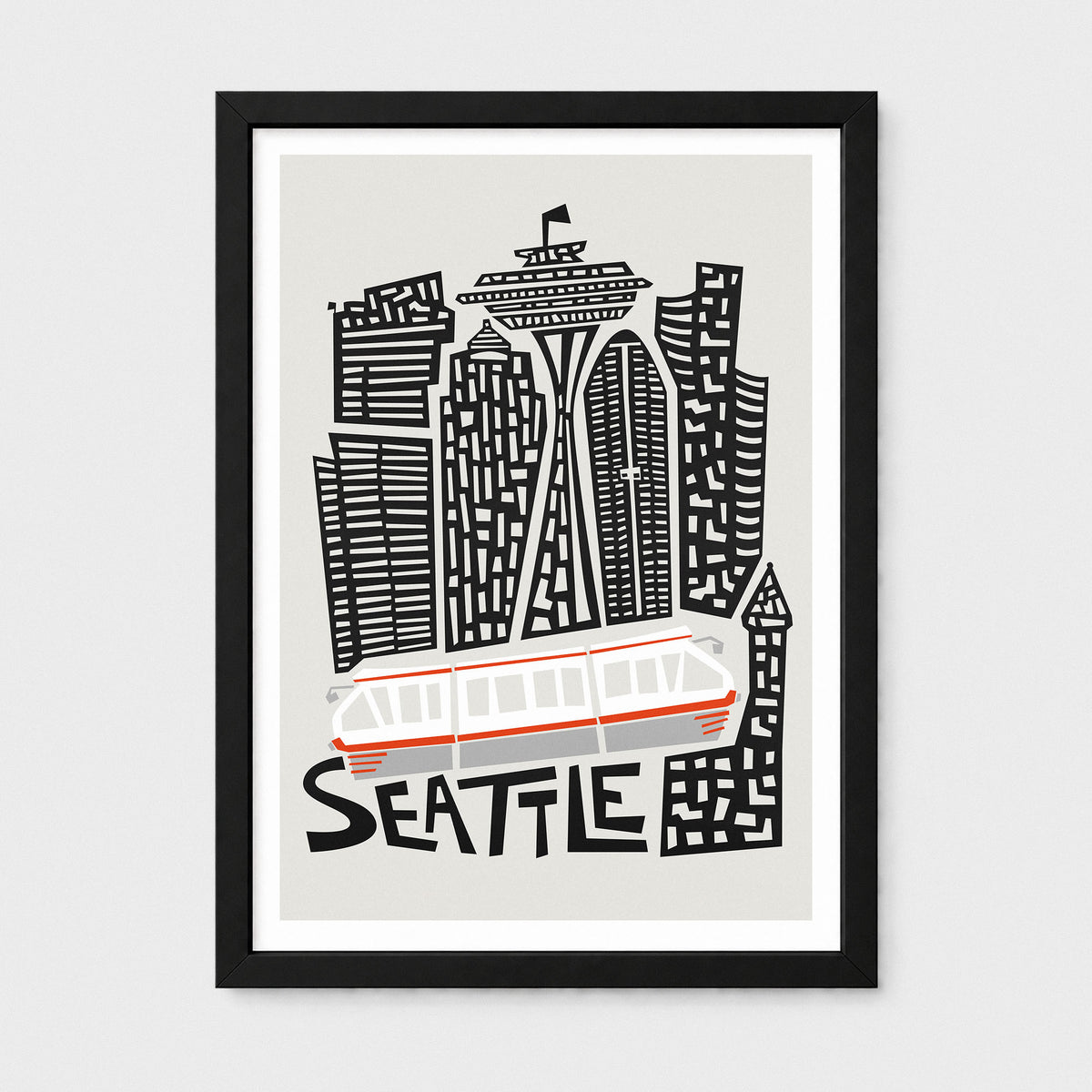 A framed Seattle cityscape art print featuring stylized black buildings, the Space Needle, a white and red tram, and the word "SEATTLE" in black on a light gray background, shown in a black frame against a light gray wall.