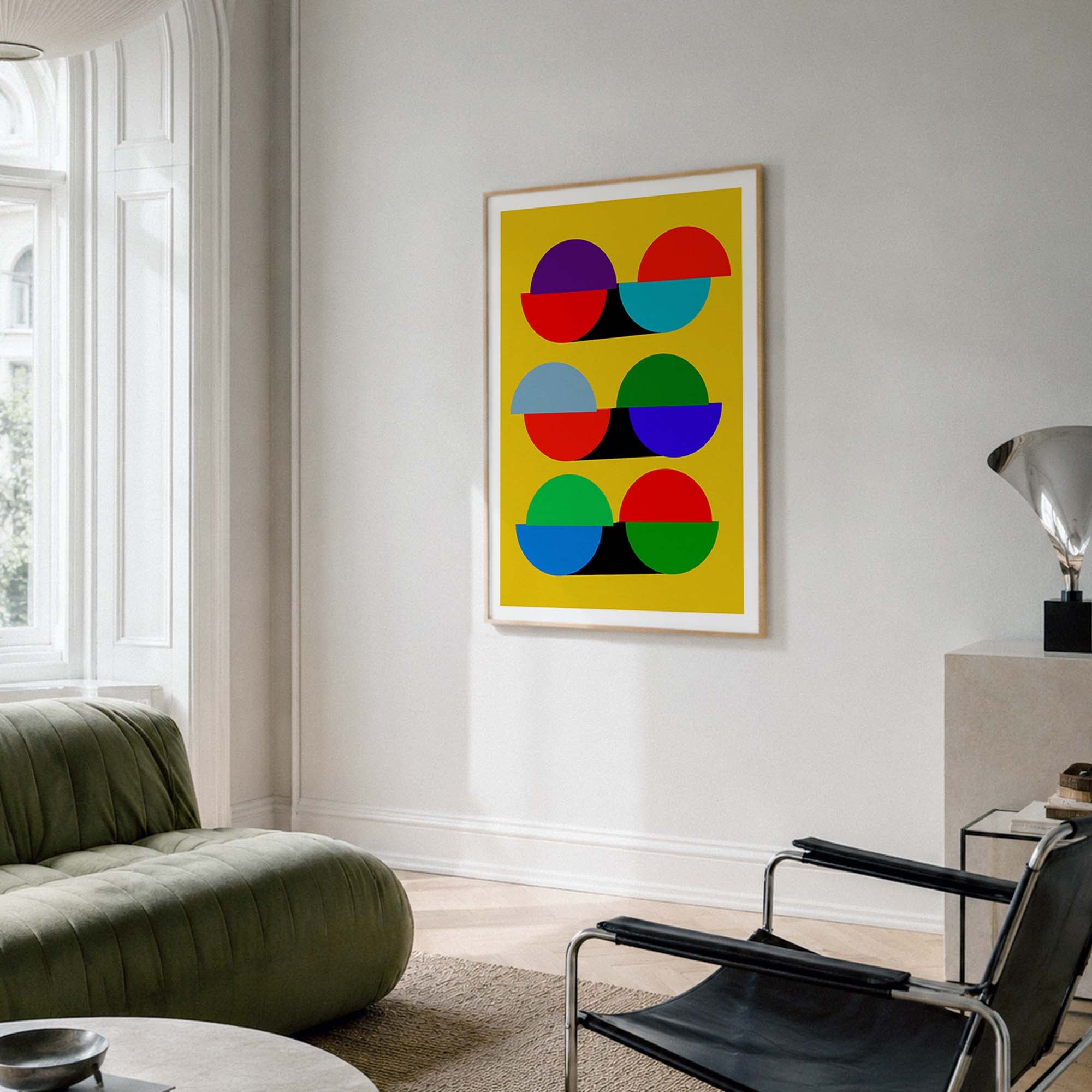 A framed abstract art print with colorful geometric semicircles on a bright yellow background, hanging on a white wall in a modern living room setting.