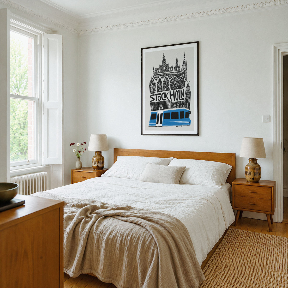 A framed black and white Stockholm cityscape poster with a blue tram hangs on a white wall above a wooden bed in a bright, modern bedroom.