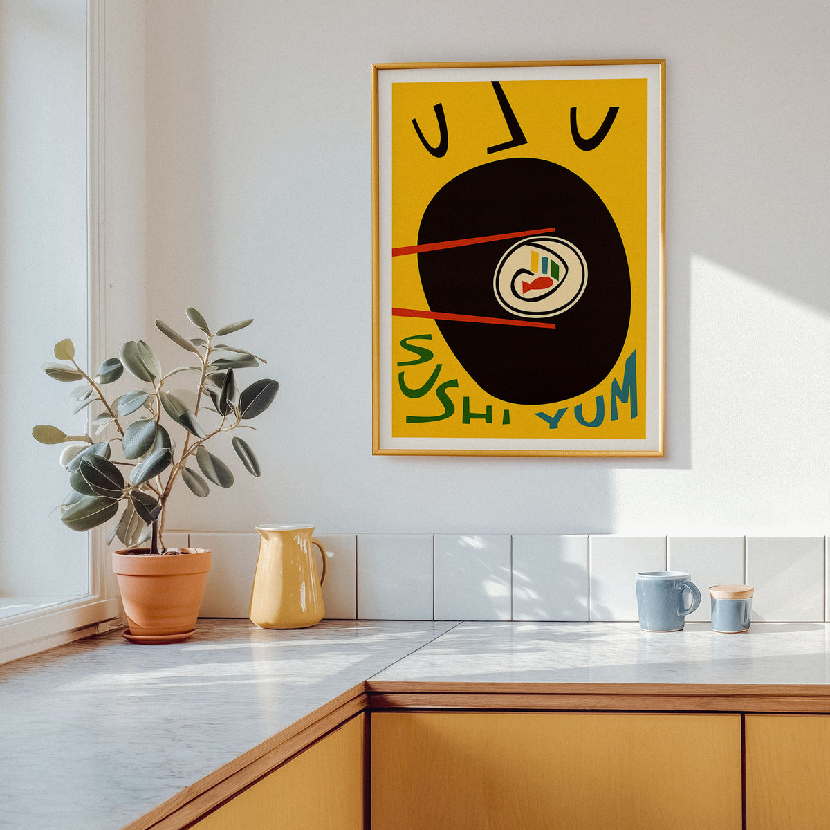 A framed abstract sushi-themed art print hangs on a white kitchen wall above a countertop, with a potted plant, yellow pitcher, and mugs nearby.
