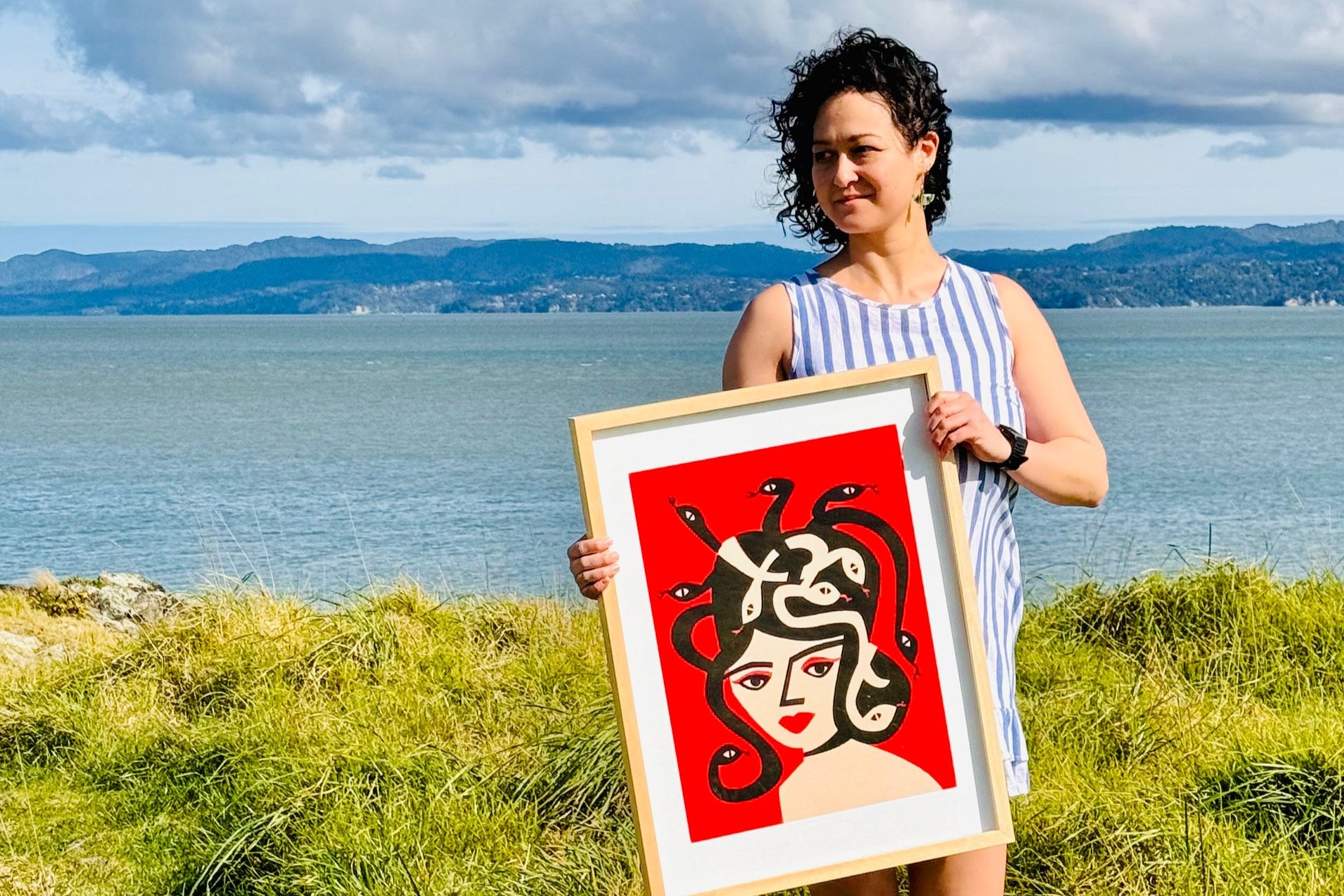 Suumin holding Medusa print with a scenic backdrop.
