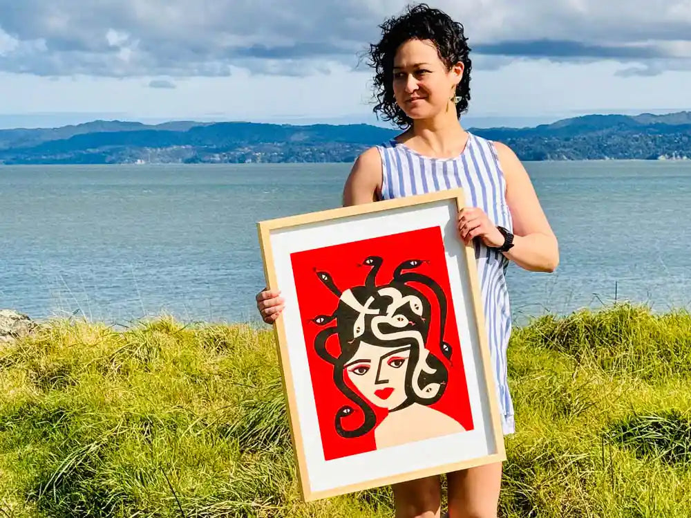 Suumin Ang of Fox & Velvet holding Medusa print with a scenic backdrop.