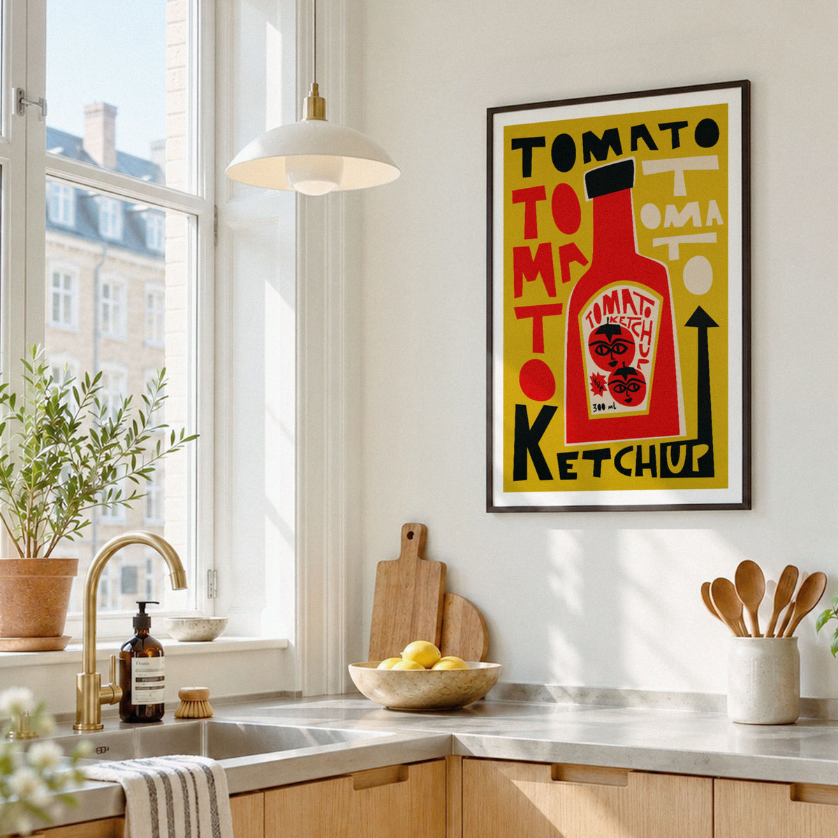 A framed pop-art style poster featuring a yellow mayonnaise can with red, black, and white typography, hanging on a white kitchen wall above a countertop with a sink, plants, and utensils.