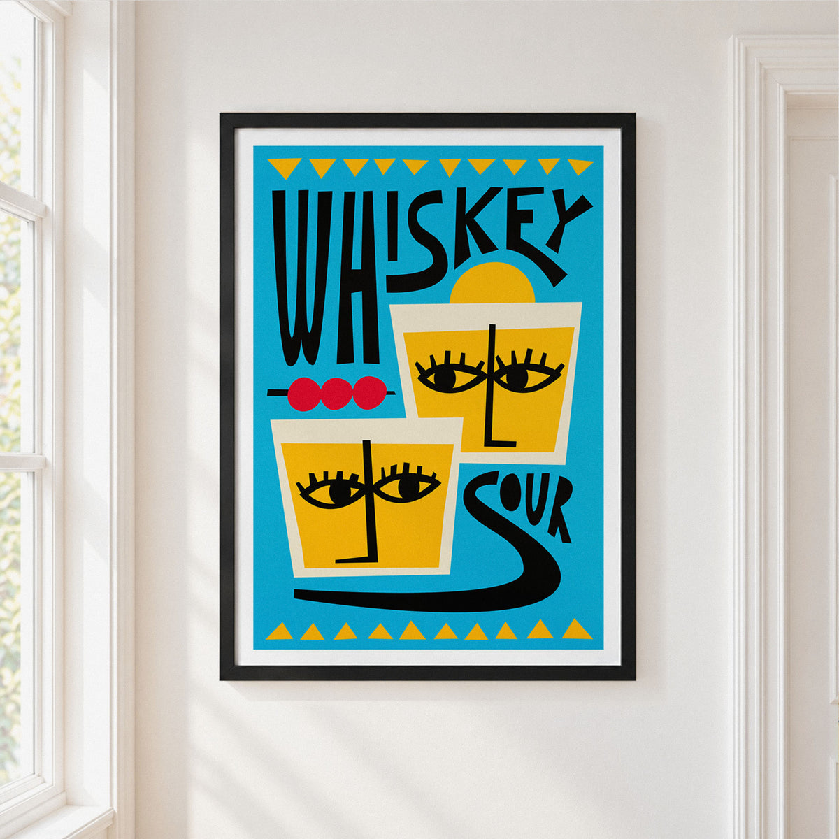 A framed art print featuring a retro-style graphic design with the words 'WHISKEY SOUR' and stylized faces in yellow, black, blue, white, and red, hung on a white wall next to a window.