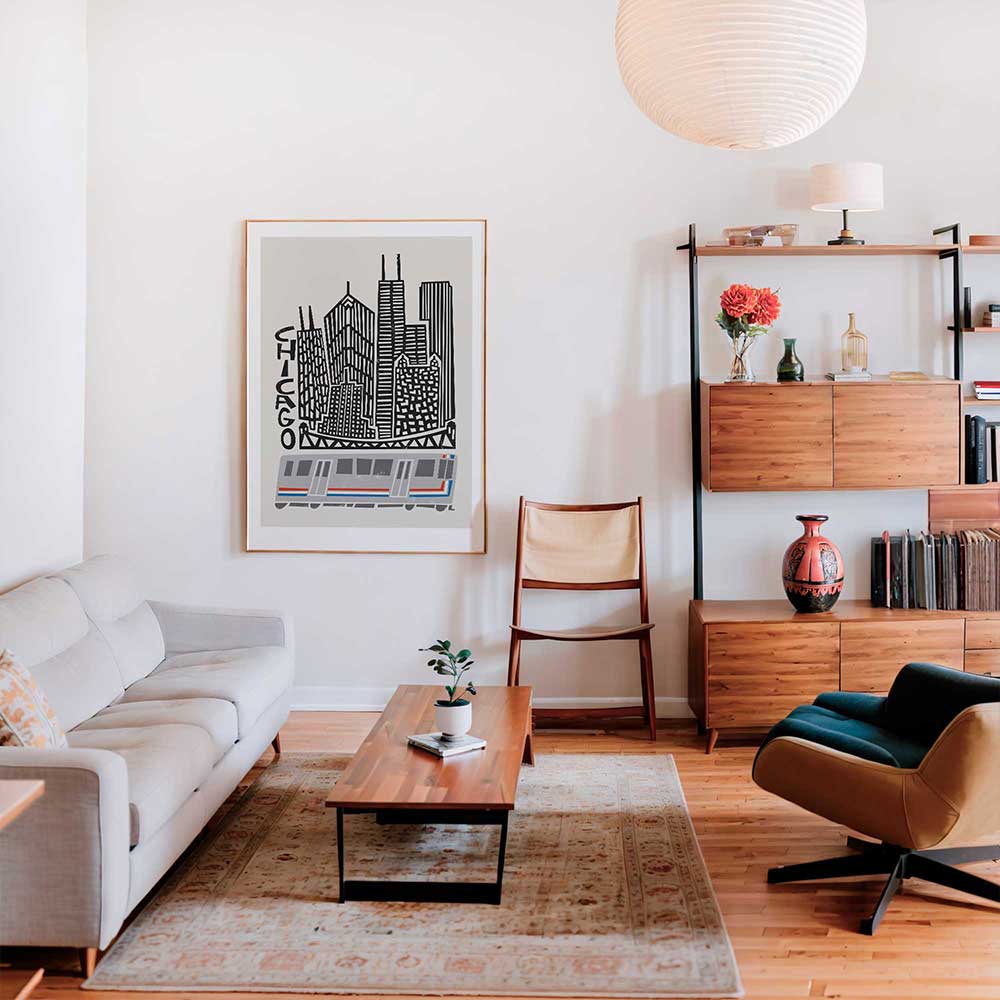 Framed Chicago cityscape print with CTA train on a pale wall in a stylish mid-century modern living room, complete with bookshelves and a minimalist aesthetic.