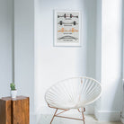 Framed famous bridges print hanging in a minimal white space with natural light and a rattan chair, giving a travel-inspired, editorial feel.