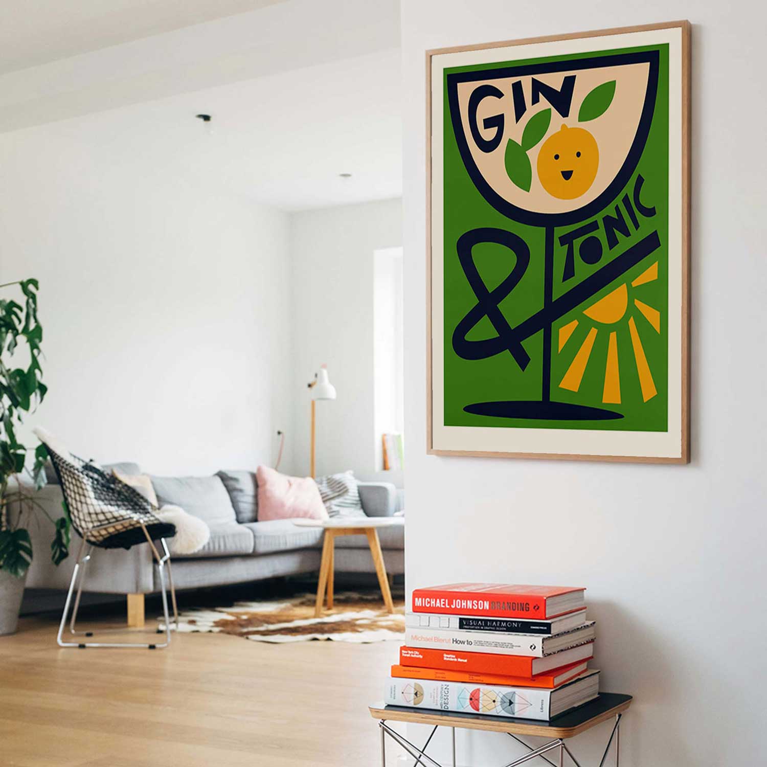A framed art print featuring a stylized green wine glass with the words 'GIN & TONIC' and a yellow citrus slice illustration, displayed on a white wall in a modern living room setting.