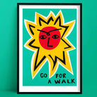 Go For a Walk Sun inspirational print, featuring a bold red sun face with yellow rays and hand-lettered text, framed on green wall.