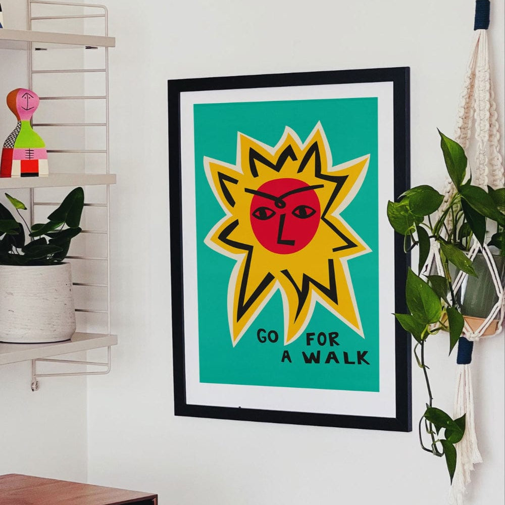 Go For a Walk poster framed above a desk in a colourful studio corner with houseplants and shelving.