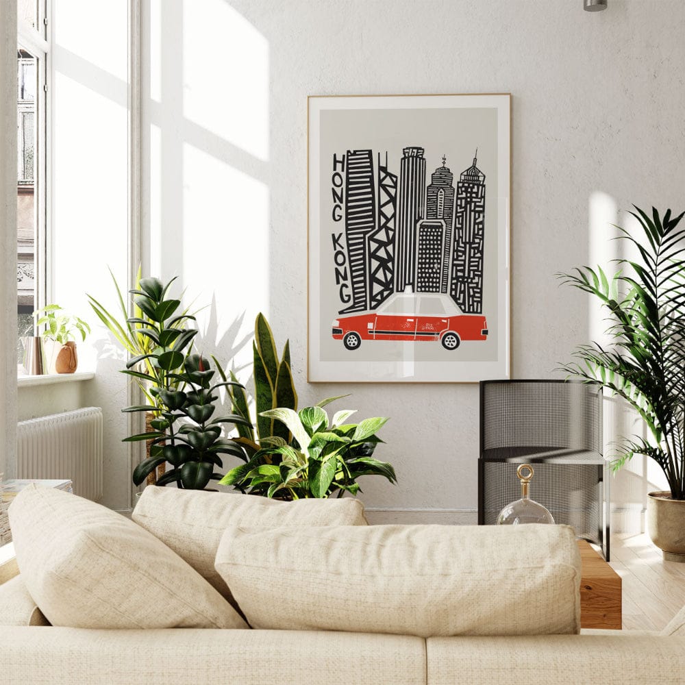 Framed Hong Kong poster wall art displayed above a cream-coloured sofa in a sunlit room, showing off bold vertical architecture and the signature red taxi below.