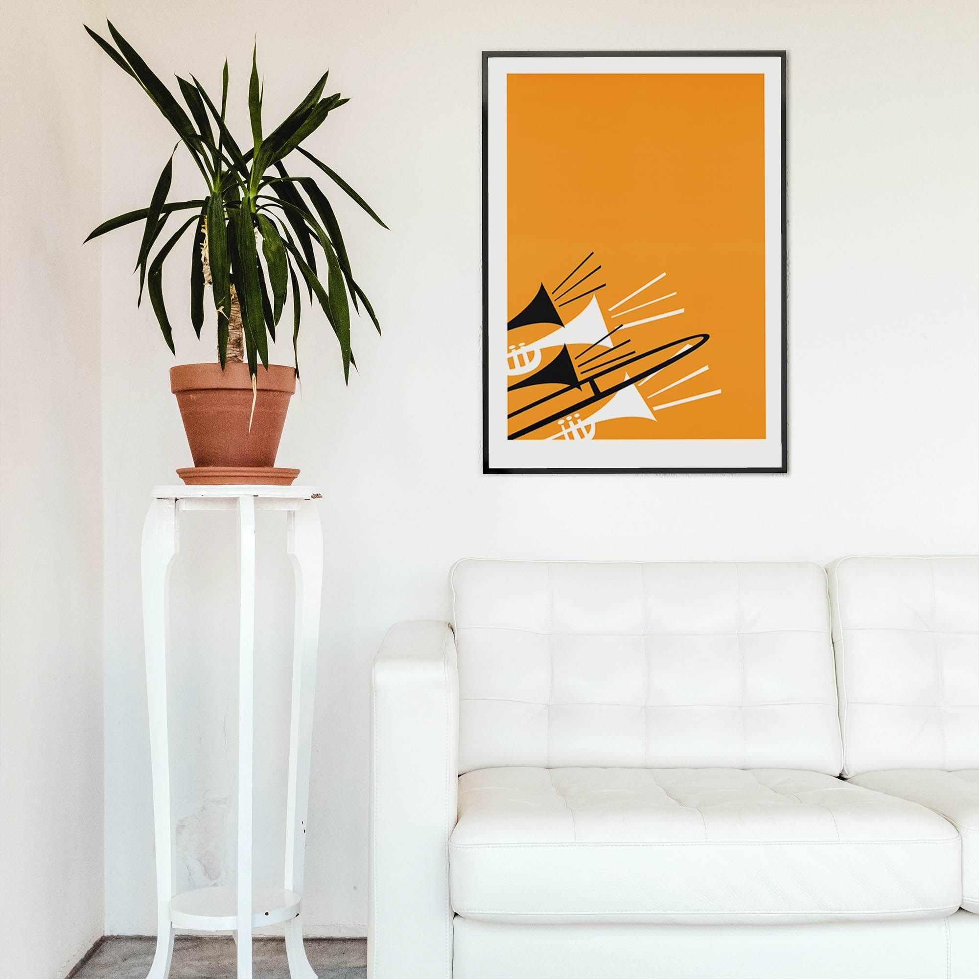 Trombone and trumpet art print hanging above a white sofa and tall plant in a minimalist room