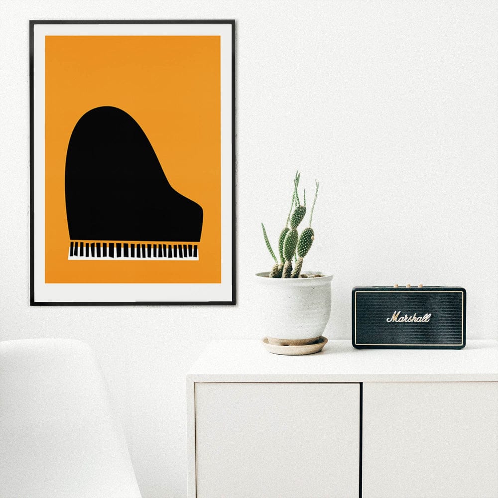 Piano art print on a white wall above a minimalist desk with small plant and speaker