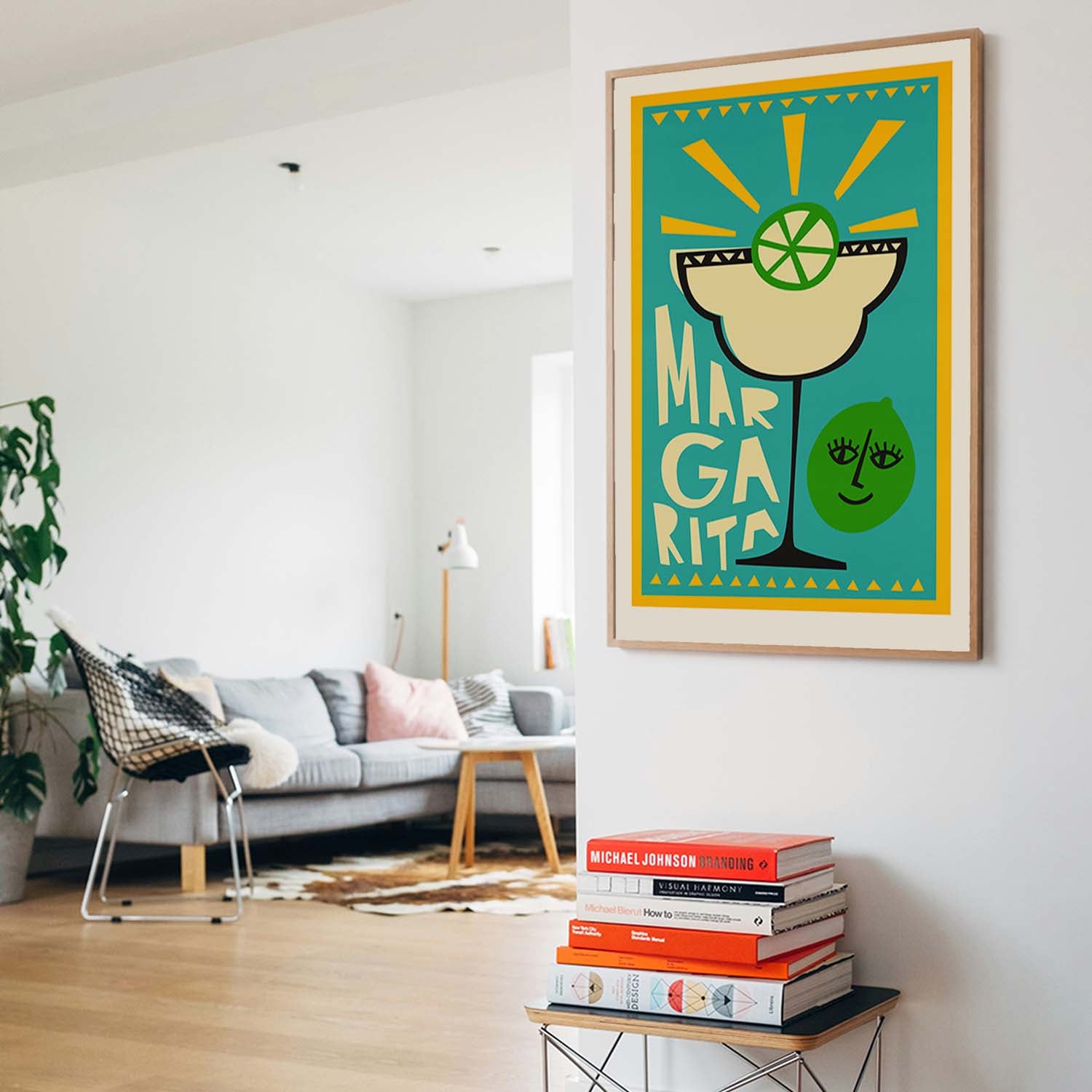 A framed art print featuring a stylized margarita glass with a lime wheel and the words 'MARGARITA' in bold lettering, hanging on a white wall in a modern living room setting.